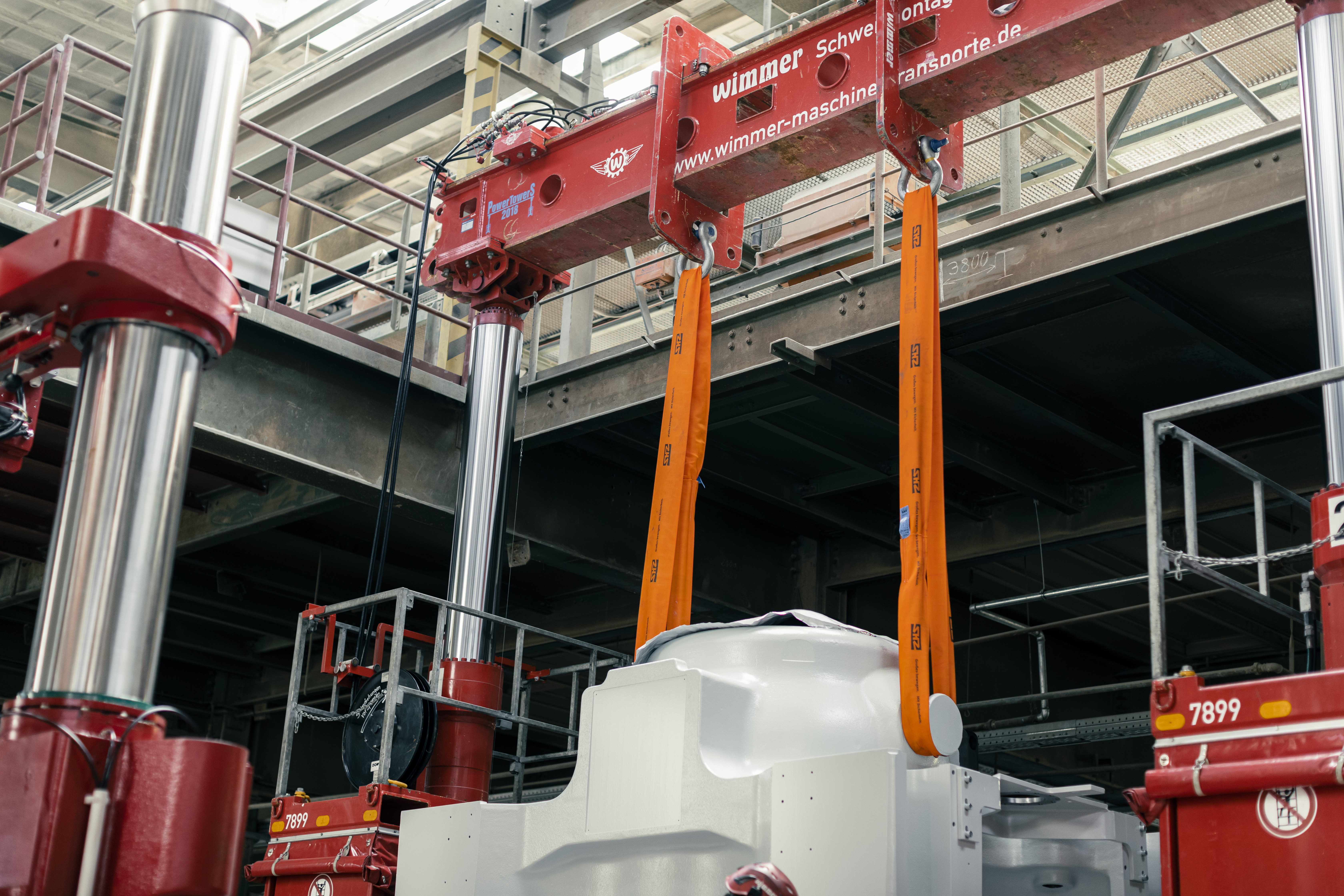 Technician performing maintenance on a large industrial crane in a mining facility with heavy equipment and machinery in the background under bright daylight, conveying a sense of professionalism and safety